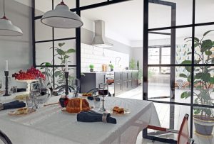 Black aluminium internal French doors with slim steel-look grid frame, opening from a dining room into a bright white kitchen.