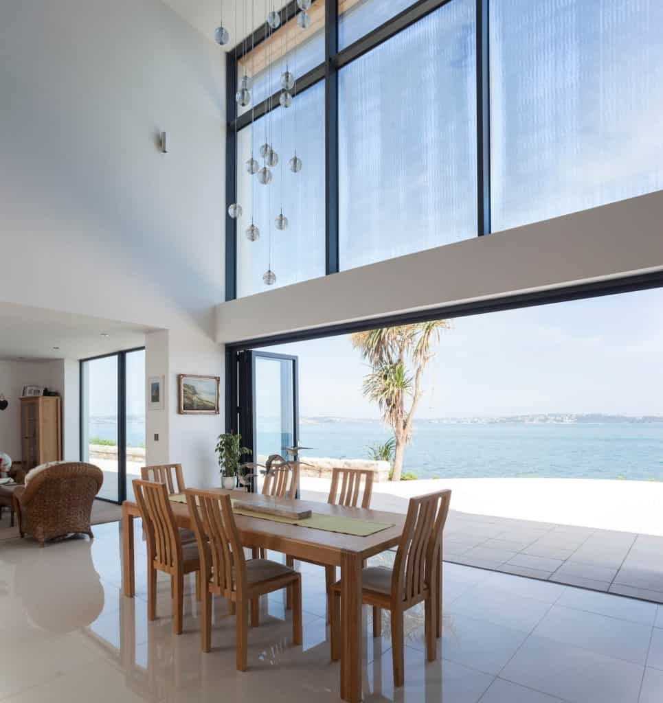 Aluminium bifold doors opening to a stunning sea view, bringing natural light into the dining area.