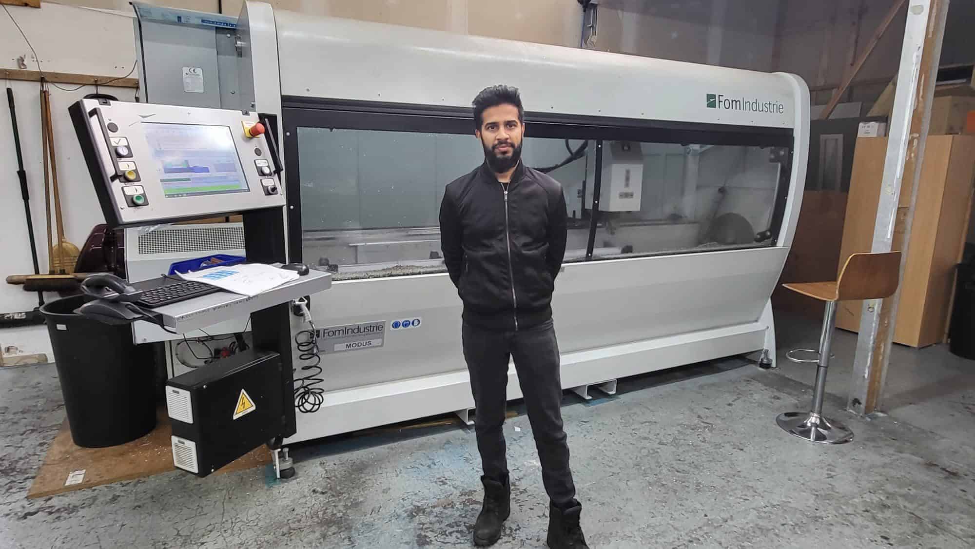 Man standing in front of advanced window manufacturing machine in workshop.