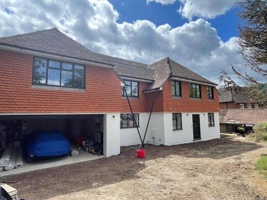 Front view of a modern detached house with black casement windows, red tiled upper walls, and a double garage with one blue car inside.