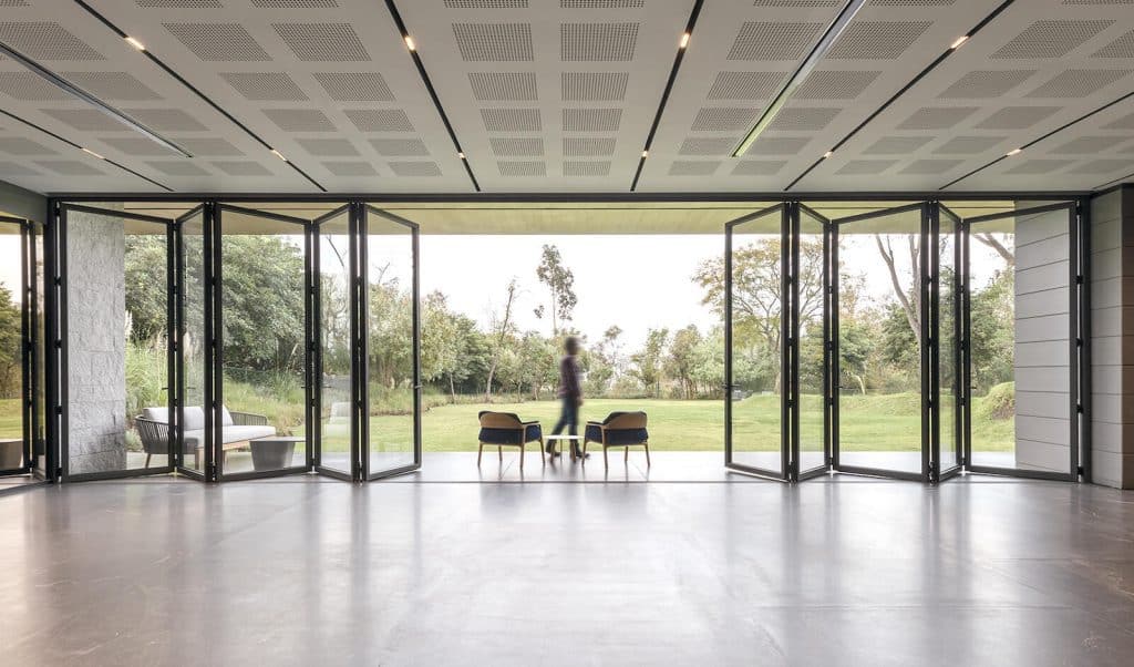 Aluminium bifold door system with large glass panels opening to a lush garden landscape.