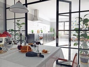 Modern kitchen viewed through black-framed aluminium internal partitions with a dining table set with wine glasses, candles, cheese, and cake in the foreground, suggesting a stylish and functional use of space in a Watford home.
