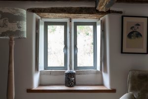 Cosy interior with exposed wooden beam, window seat, and decorative lamp.