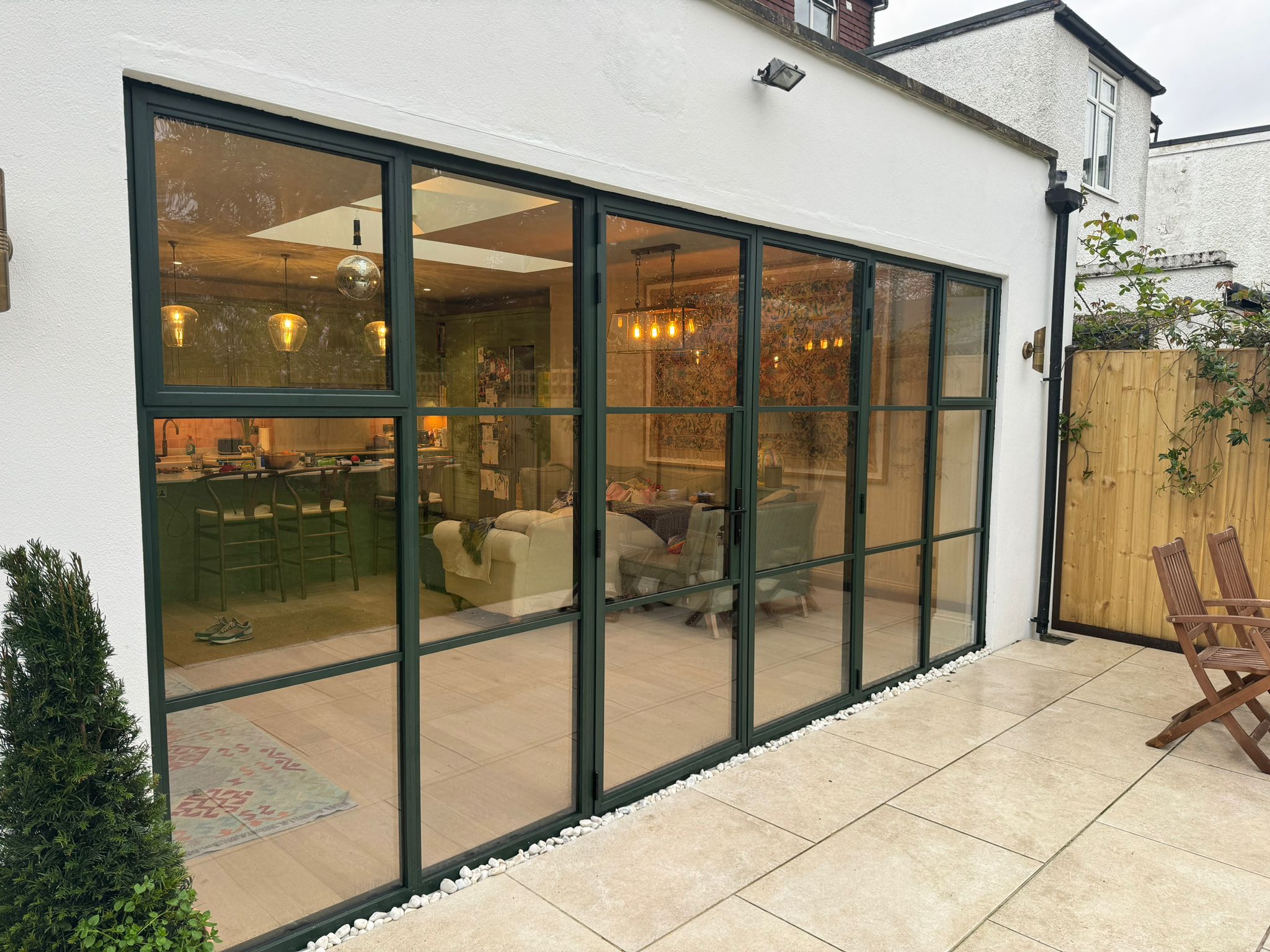 Steel look doors with slim black aluminium frames and glazing bars opening from a living area to a tiled patio.